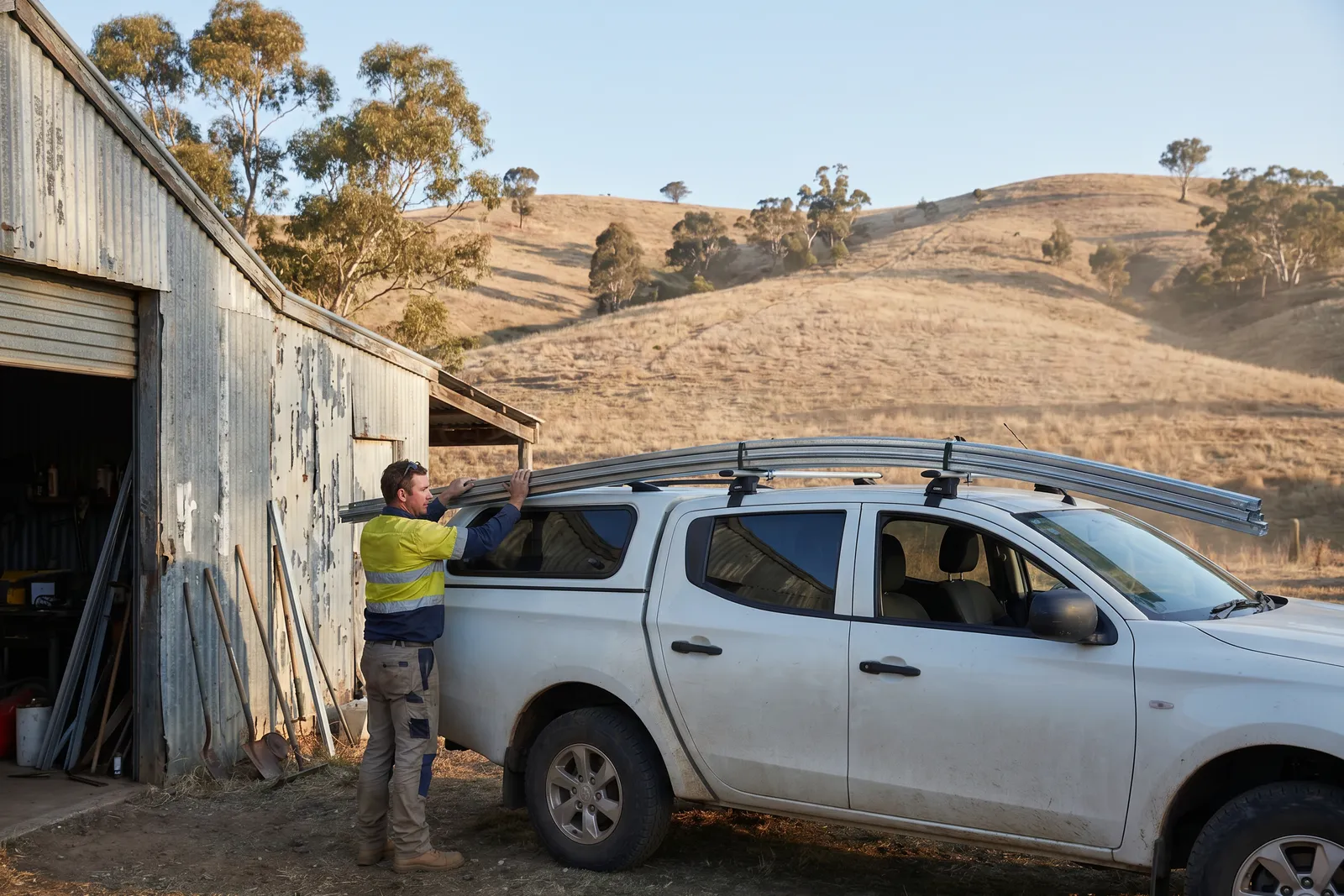 A technician loading door track onto ute roof racks outside a country workshop