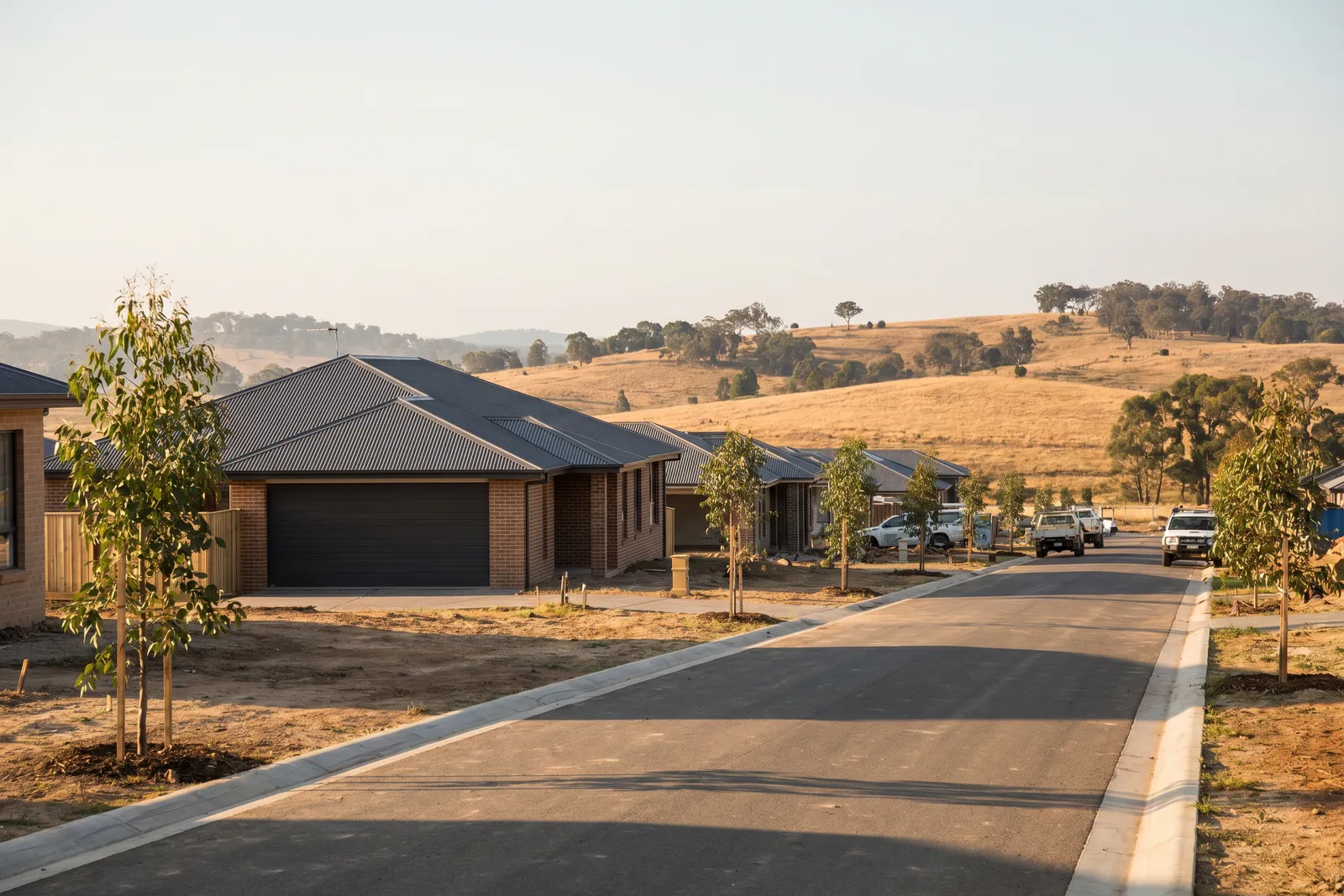 New homes with sectional garage doors on a fresh estate street, dry hills behind
