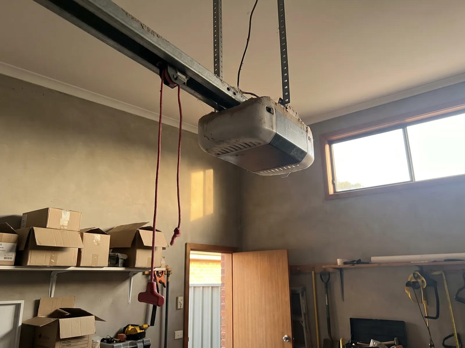 A ceiling-mounted garage door opener and rail with its red manual release cord
