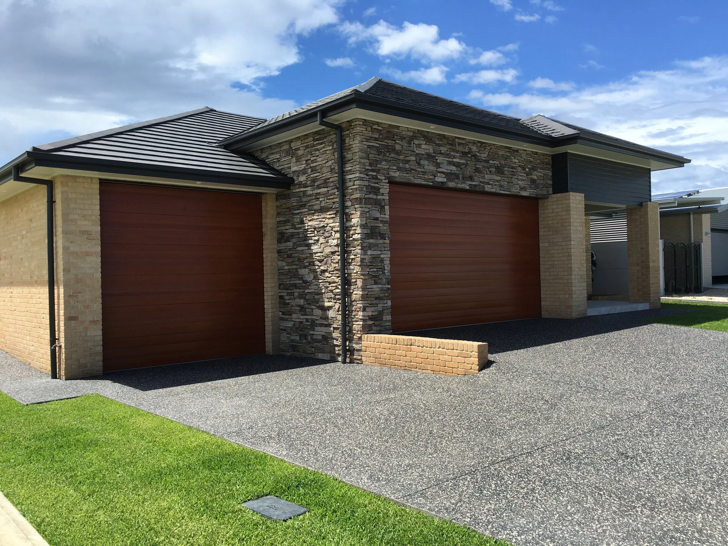 Two wood-look sectional garage doors installed on a modern home featuring a mix of brick and stone masonry.